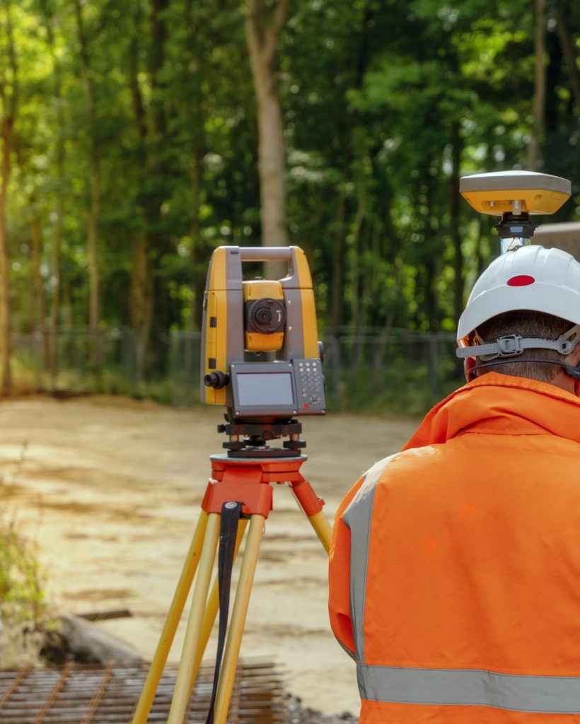 Surveyor site engineer with total positioning station on the construction site of the new road construction with construction machinery and materials  in the background